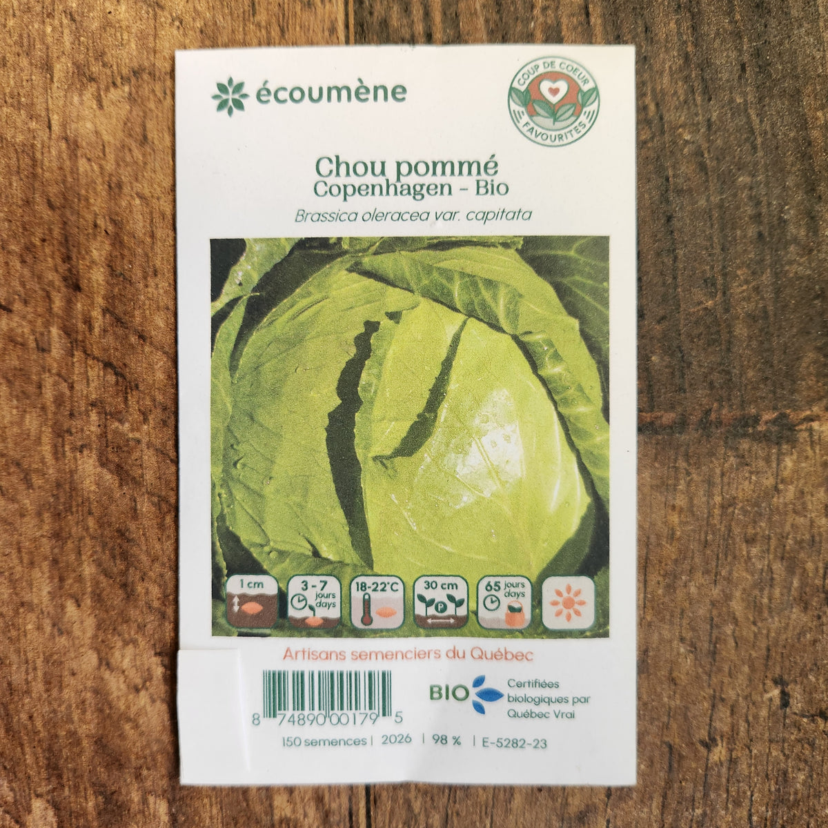 Sachet de semences Chou pommé Copenhagen. Emballage blanc photographié de face sur un fond de bois brun. Une image du végétal occupe la partie centrale, sous le nom imprimé. De petits pictogrammes et un code-barres apparaissent au bas du sachet. La marque Écoumène figure dans la partie supérieure de cette présentation.