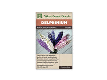 Sachet Magic Fountains Mix de West Coast Seeds sur fond blanc. Un vase contient des hampes de fleurs lavande, blanches, bleues et roses devant des planches pâles. Les petits centres contrastent avec les pétales. Des boutons restent fermés au sommet. Le bandeau orangé indique Delphinium, puis la bande brune porte le nom du mélange et FL2080.