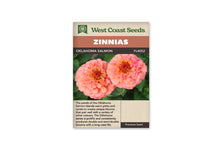 Sachet West Coast Seeds Oklahoma Salmon avec deux fleurs rondes rose saumon vues de face. Les pétales sont rangés en cercles autour de centres rouges bordés de petites fleurs jaunes. Les feuilles vertes forment le fond de la photo. Le nom est inscrit sur le bandeau brun, sous le titre blanc sur fond orange.