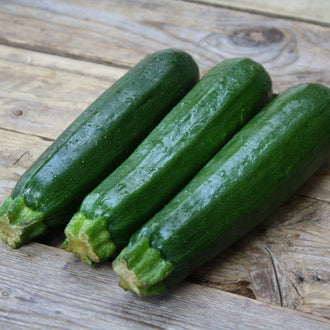 Courgette Dark Green. Courgettes vert foncé allongées déposées sur du bois. Le cadrage permet de voir les formes, les couleurs et les détails du sujet représenté. Les contours se détachent du fond de l’image, avec des différences de teinte et de texture visibles sur les surfaces. Cette vue accompagne la présentation du produit dans la boutique.