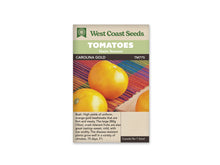 Sachet West Coast Seeds avec les mentions Tomatoes, Main Season et Carolina Gold. La photo montre des tomates rondes jaune orangé sur un tissu rayé de plusieurs couleurs. Une partie de fruit coupé est visible au bord droit. Le nom de la variété et le code TM775 figurent sous les bandeaux verts de la marque.