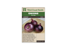 Trois oignons rouges sont posés sur une planche de bois, devant un arrière-plan clair. Les enveloppes foncées présentent des reflets pourpres et des zones plus brillantes. Les bulbes sont arrondis, avec des cols courts et secs. Le sachet de West Coast Seeds identifie la variété Cabernet et montre les oignons entiers sans coupe de la chair.