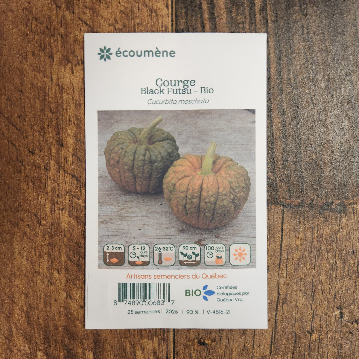 Sachet de semences Courge Black Futsu. Emballage blanc photographié de face sur un fond de bois brun. Une image du végétal occupe la partie centrale, sous le nom imprimé. De petits pictogrammes et un code-barres apparaissent au bas du sachet. La marque Écoumène figure dans la partie supérieure de cette présentation.