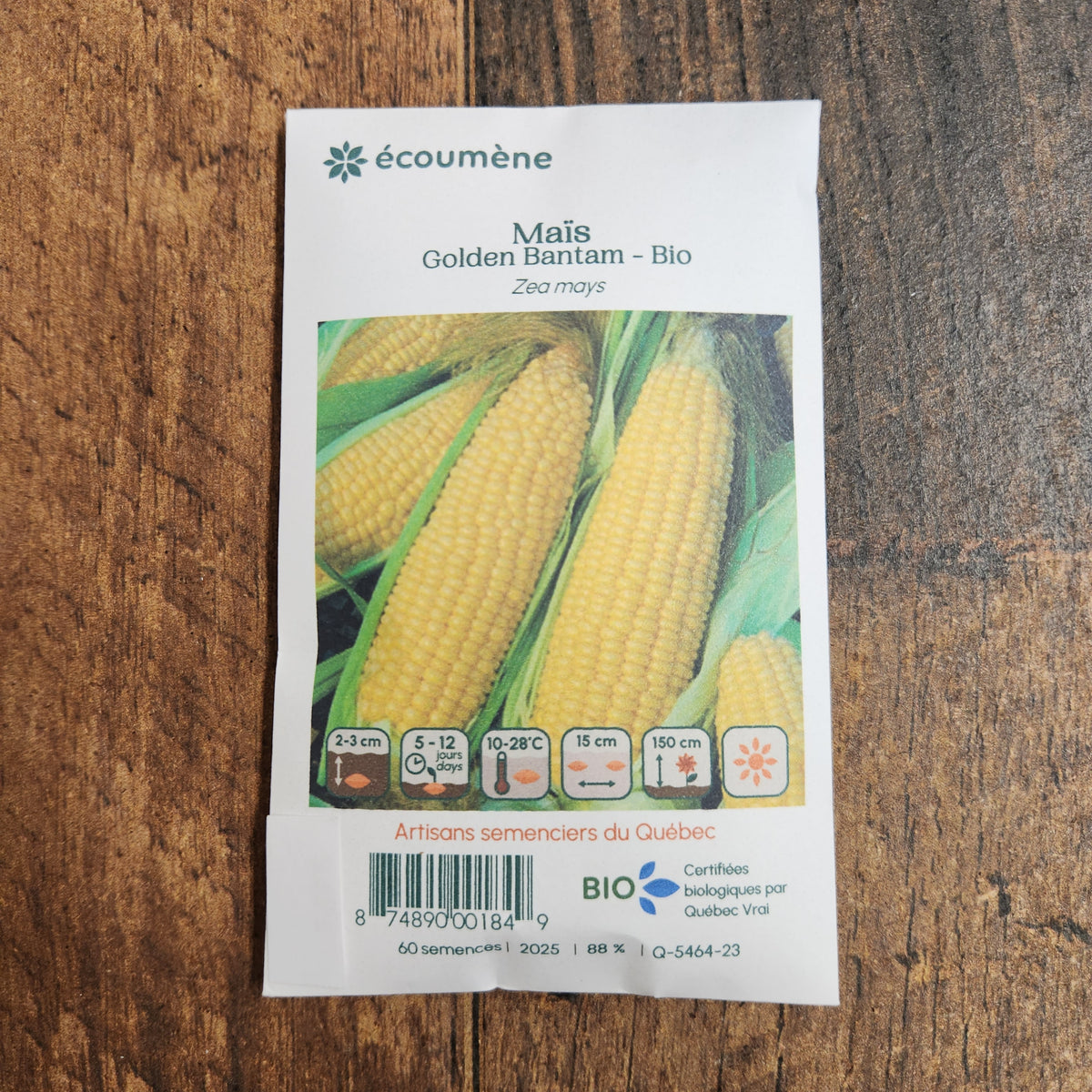 Sachet de semences Maïs Golden Bantam. Emballage blanc photographié de face sur un fond de bois brun. Une image du végétal occupe la partie centrale, sous le nom imprimé. De petits pictogrammes et un code-barres apparaissent au bas du sachet. La marque Écoumène figure dans la partie supérieure de cette présentation.