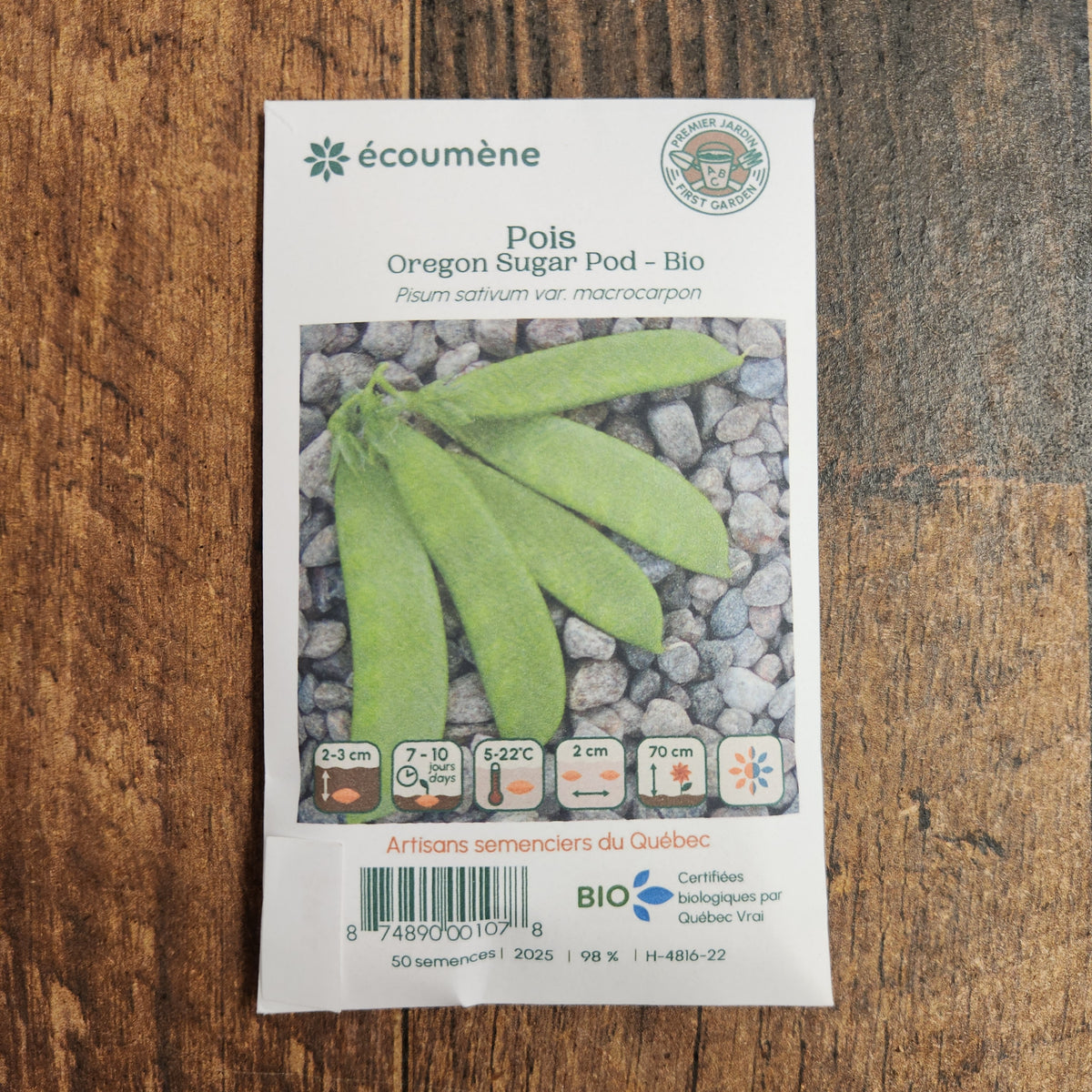 Sachet de semences Pois Oregon Sugar Pod. Emballage blanc photographié de face sur un fond de bois brun. Une image du végétal occupe la partie centrale, sous le nom imprimé. De petits pictogrammes et un code-barres apparaissent au bas du sachet. La marque Écoumène figure dans la partie supérieure de cette présentation.