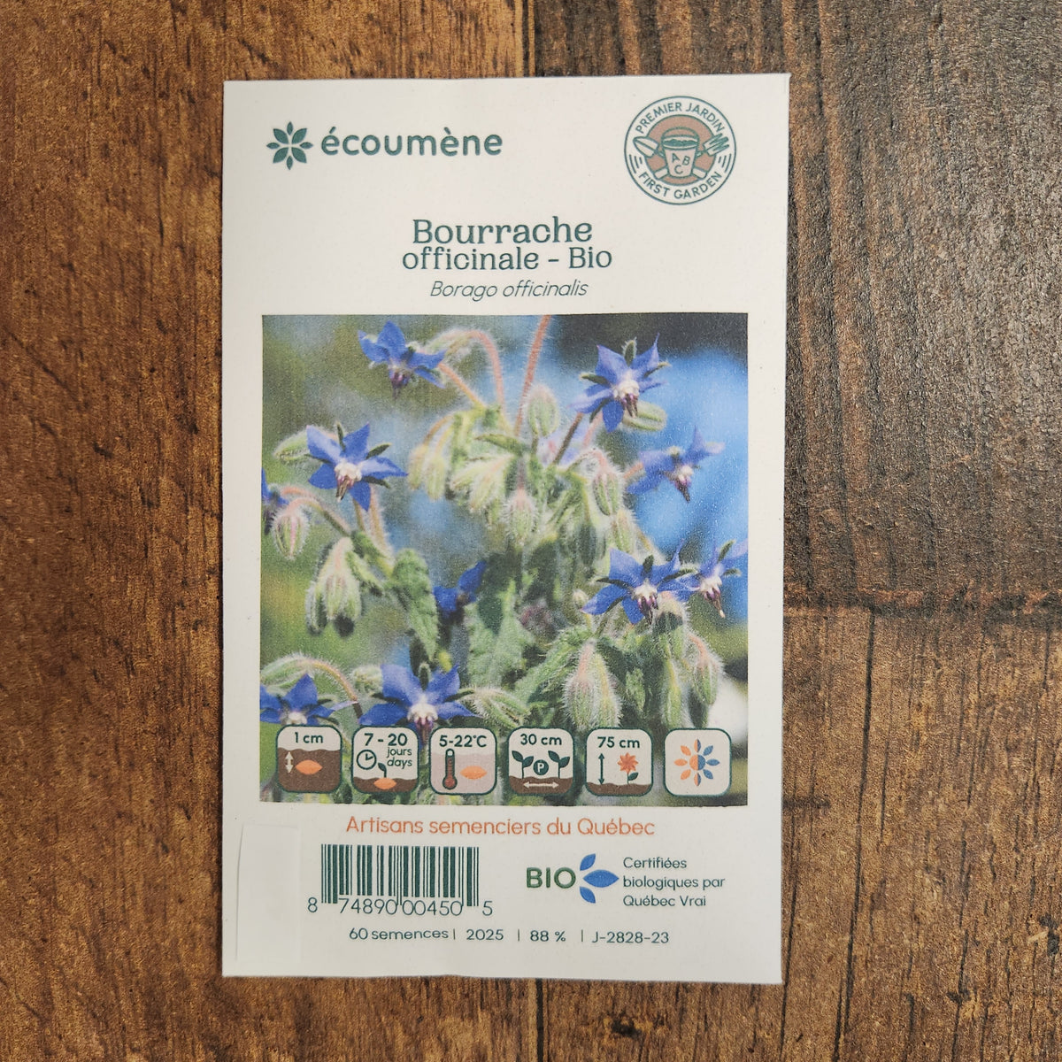 Sachet de semences Bourrache officinale. Emballage blanc photographié de face sur un fond de bois brun. Une image du végétal occupe la partie centrale, sous le nom imprimé. De petits pictogrammes et un code-barres apparaissent au bas du sachet. La marque Écoumène figure dans la partie supérieure de cette présentation.