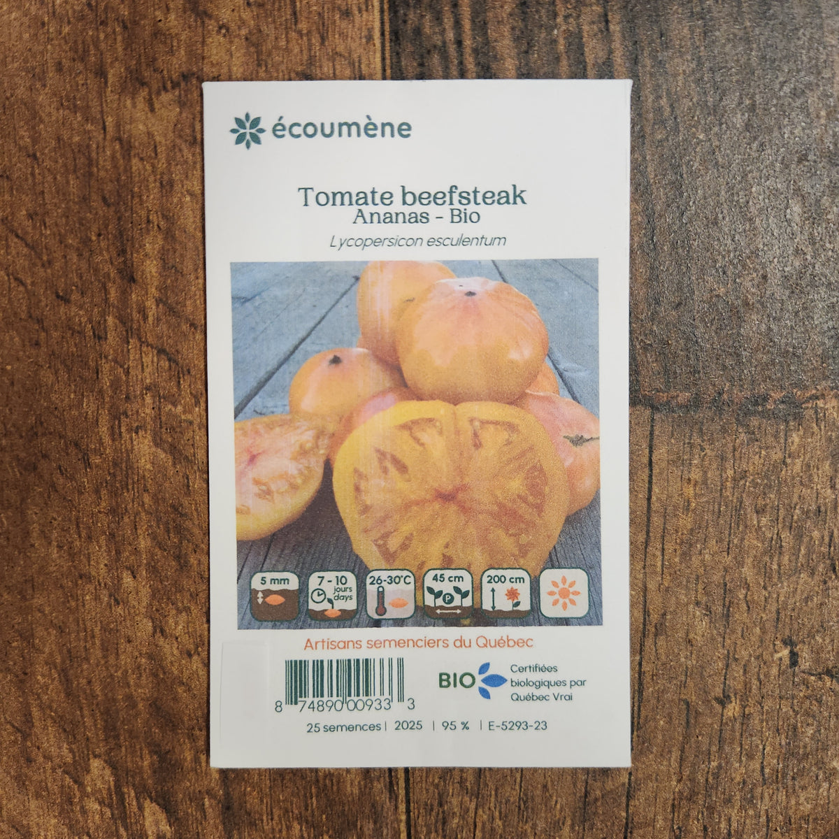 Sachet de semences Tomate Beefsteak Ananas. Emballage blanc photographié de face sur un fond de bois brun. Une image du végétal occupe la partie centrale, sous le nom imprimé. De petits pictogrammes et un code-barres apparaissent au bas du sachet. La marque Écoumène figure dans la partie supérieure de cette présentation.