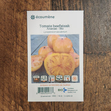 Sachet de semences Tomate Beefsteak Ananas. Emballage blanc photographié de face sur un fond de bois brun. Une image du végétal occupe la partie centrale, sous le nom imprimé. De petits pictogrammes et un code-barres apparaissent au bas du sachet. La marque Écoumène figure dans la partie supérieure de cette présentation.