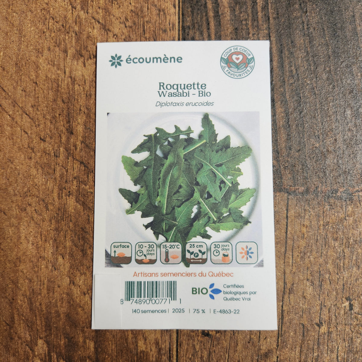 Sachet de semences Roquette Japonaise Wasabi. Emballage blanc photographié de face sur un fond de bois brun. Une image du végétal occupe la partie centrale, sous le nom imprimé. De petits pictogrammes et un code-barres apparaissent au bas du sachet. La marque Écoumène figure dans la partie supérieure de cette présentation.