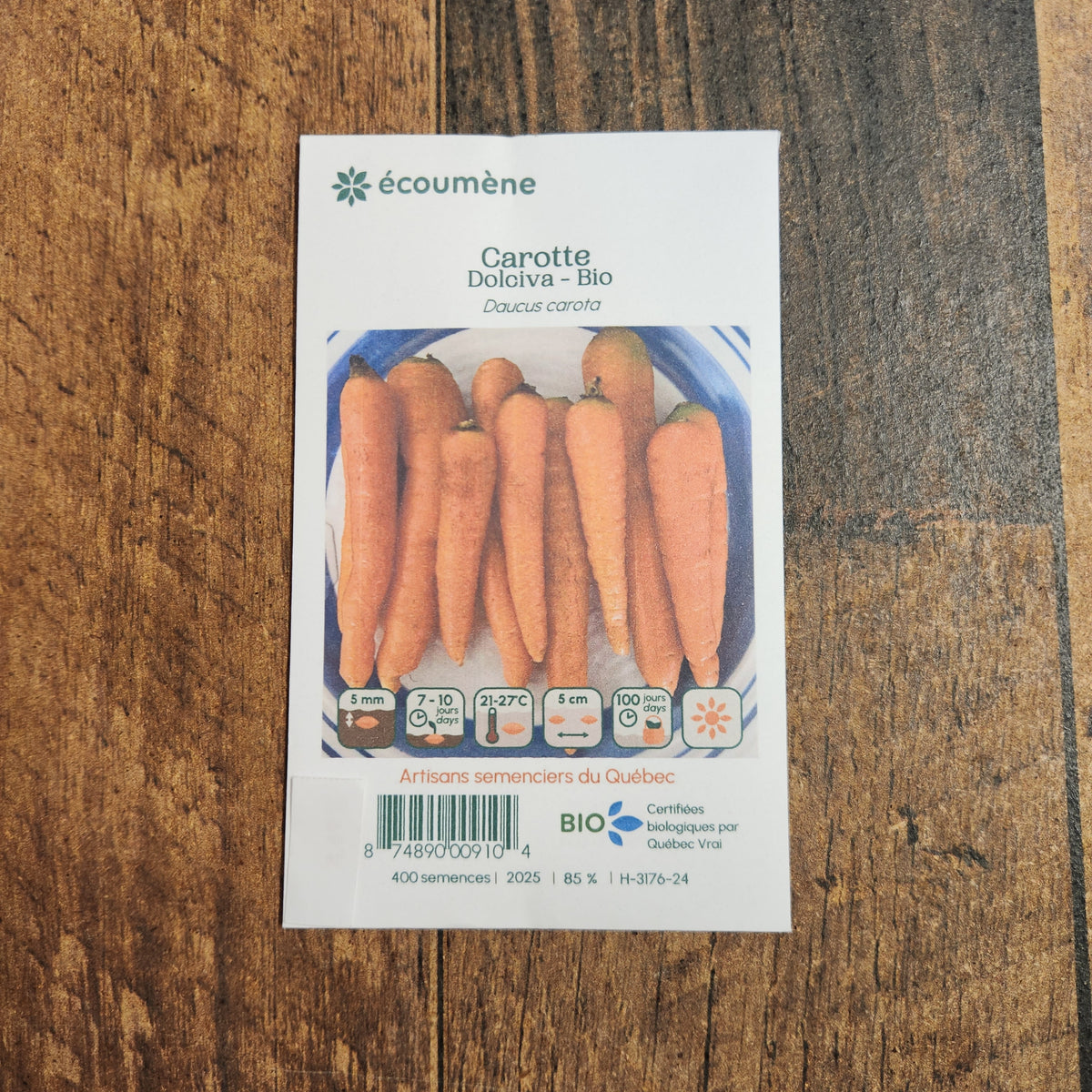 Sachet de semences Carotte Dolciva. Emballage blanc photographié de face sur un fond de bois brun. Une image du végétal occupe la partie centrale, sous le nom imprimé. De petits pictogrammes et un code-barres apparaissent au bas du sachet. La marque Écoumène figure dans la partie supérieure de cette présentation.