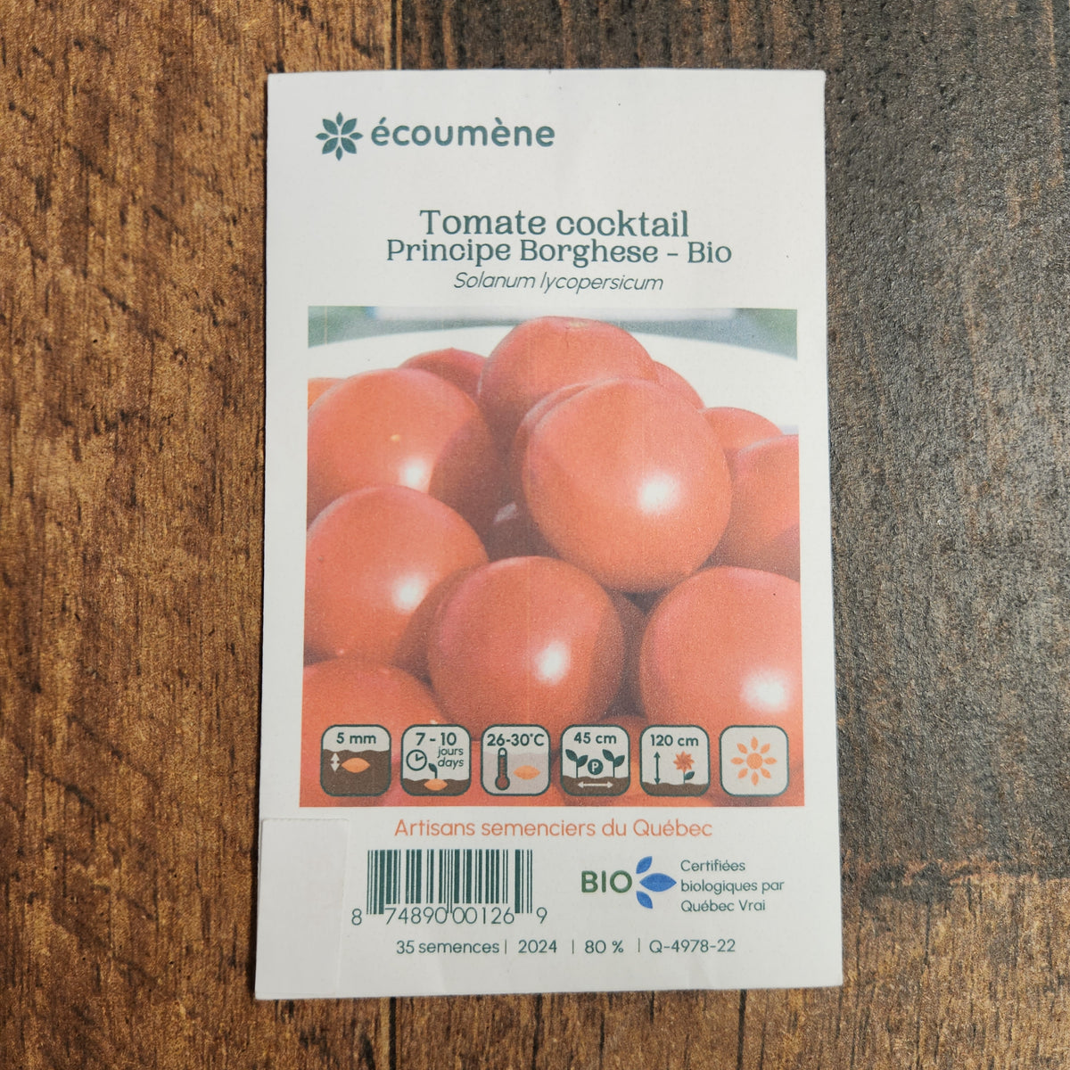 Sachet de semences Tomate Cocktail Principe Borghese. Emballage blanc photographié de face sur un fond de bois brun. Une image du végétal occupe la partie centrale, sous le nom imprimé. De petits pictogrammes et un code-barres apparaissent au bas du sachet. La marque Écoumène figure dans la partie supérieure de cette présentation.