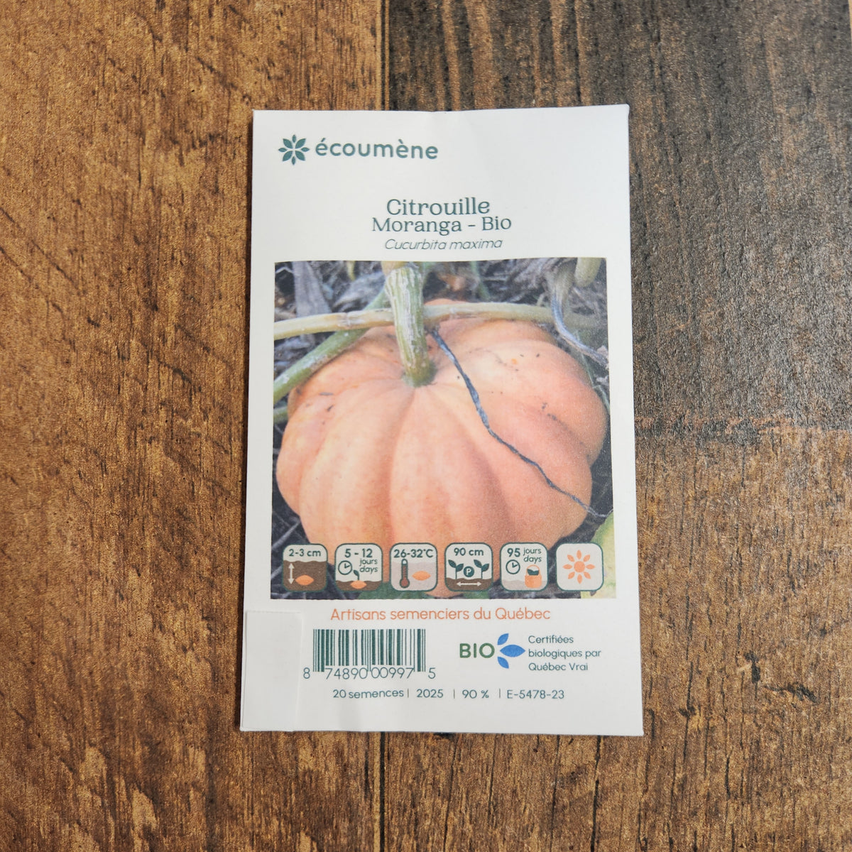 Sachet de semences Citrouille Moranga. Emballage blanc photographié de face sur un fond de bois brun. Une image du végétal occupe la partie centrale, sous le nom imprimé. De petits pictogrammes et un code-barres apparaissent au bas du sachet. La marque Écoumène figure dans la partie supérieure de cette présentation.