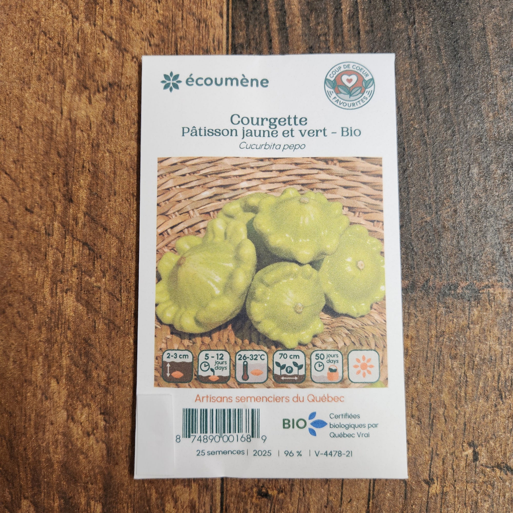 Sachet de semences Pâtisson mélange jaune et vert. Emballage blanc photographié de face sur un fond de bois brun. Une image du végétal occupe la partie centrale, sous le nom imprimé. De petits pictogrammes et un code-barres apparaissent au bas du sachet. La marque Écoumène figure dans la partie supérieure de cette présentation.