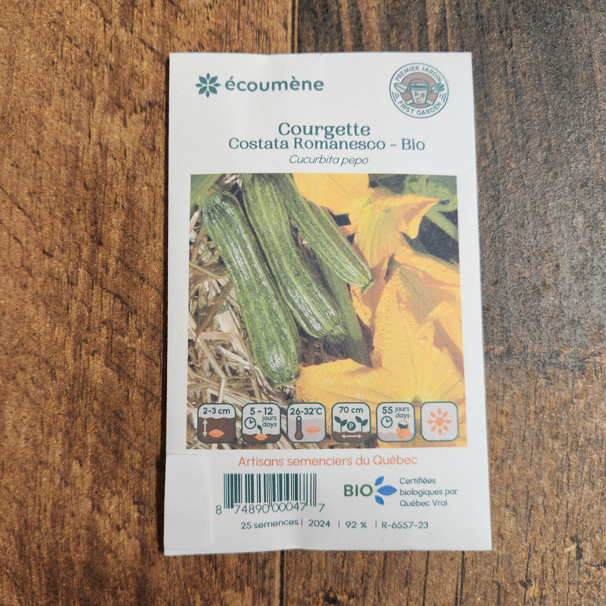 Sachet de semences Courgette Costata Romanesco. Emballage blanc photographié de face sur un fond de bois brun. Une image du végétal occupe la partie centrale, sous le nom imprimé. De petits pictogrammes et un code-barres apparaissent au bas du sachet. La marque Écoumène figure dans la partie supérieure de cette présentation.