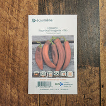 Sachet de semences Piment fort Paprika Hongrois. Emballage blanc photographié de face sur un fond de bois brun. Une image du végétal occupe la partie centrale, sous le nom imprimé. De petits pictogrammes et un code-barres apparaissent au bas du sachet. La marque Écoumène figure dans la partie supérieure de cette présentation.