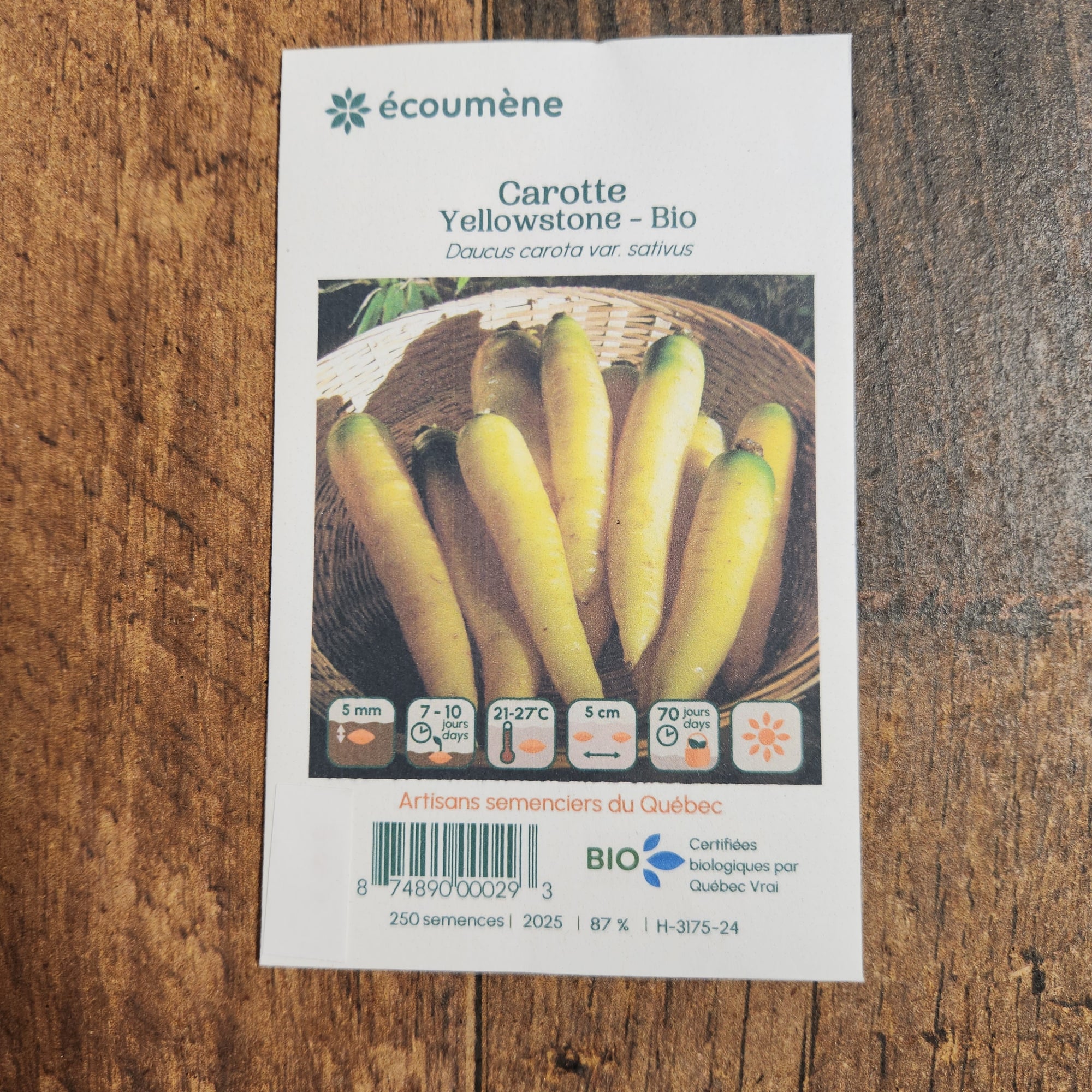 Sachet de semences Carotte jaune Yellowstone. Emballage blanc photographié de face sur un fond de bois brun. Une image du végétal occupe la partie centrale, sous le nom imprimé. De petits pictogrammes et un code-barres apparaissent au bas du sachet. La marque Écoumène figure dans la partie supérieure de cette présentation.