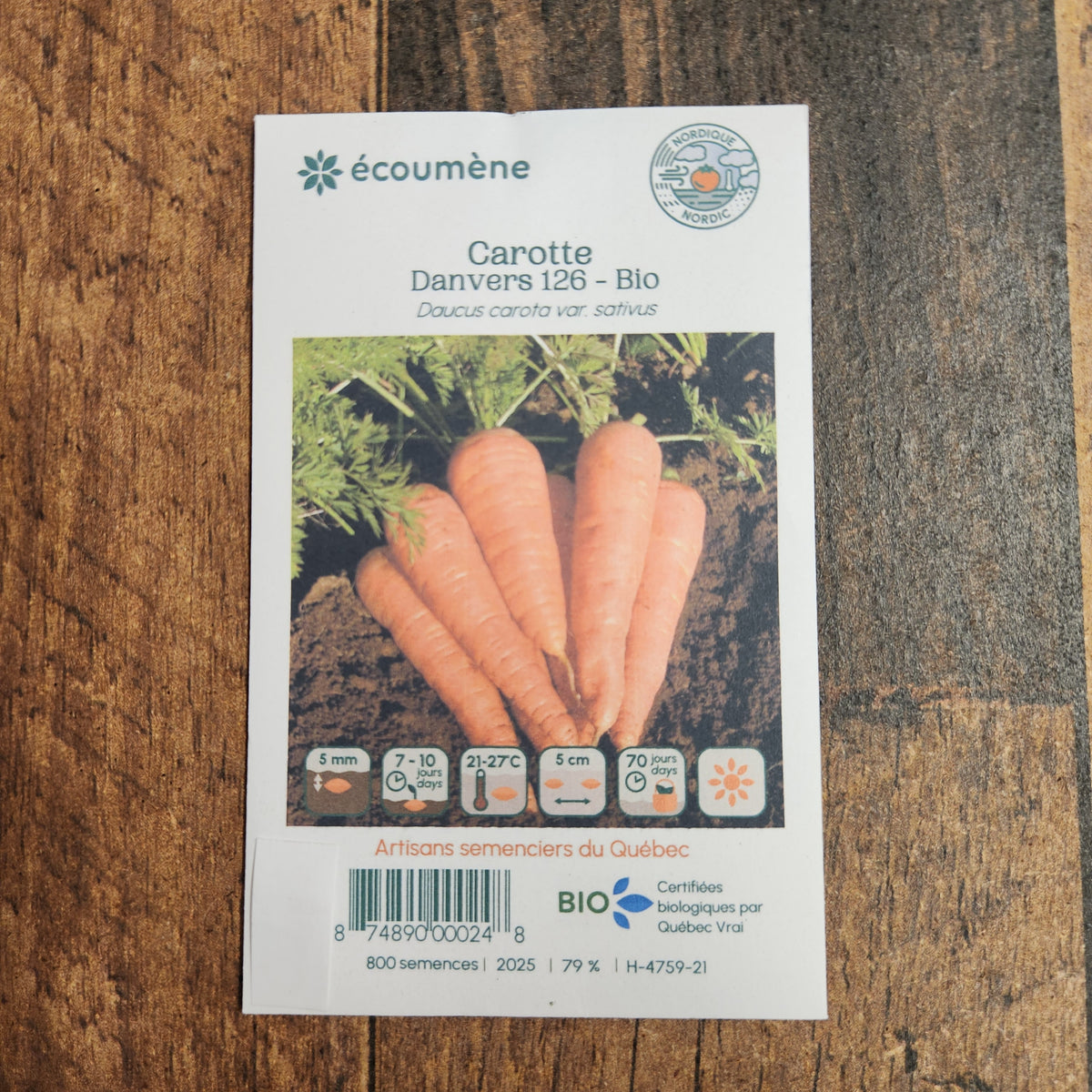 Sachet de semences Carotte Danvers 126. Emballage blanc photographié de face sur un fond de bois brun. Une image du végétal occupe la partie centrale, sous le nom imprimé. De petits pictogrammes et un code-barres apparaissent au bas du sachet. La marque Écoumène figure dans la partie supérieure de cette présentation.