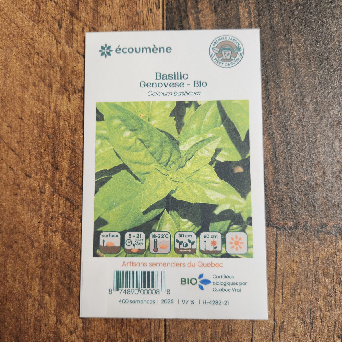 Sachet de semences Basilic Genovese. Emballage blanc photographié de face sur un fond de bois brun. Une image du végétal occupe la partie centrale, sous le nom imprimé. De petits pictogrammes et un code-barres apparaissent au bas du sachet. La marque Écoumène figure dans la partie supérieure de cette présentation.